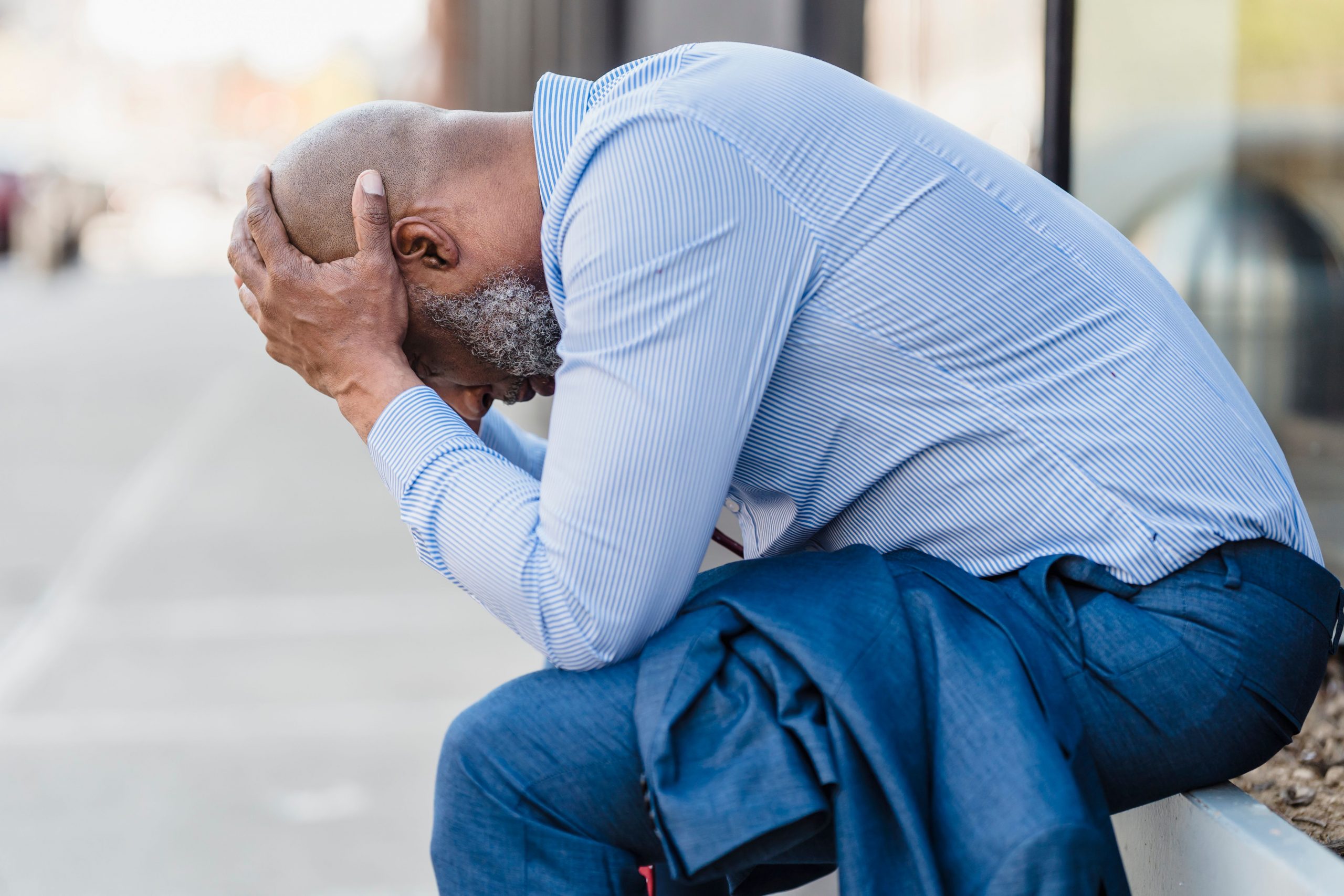 stressed man sitting outdoors, with his head in his hands