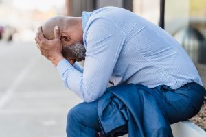 stressed man sitting outdoors, with his head in his hands
